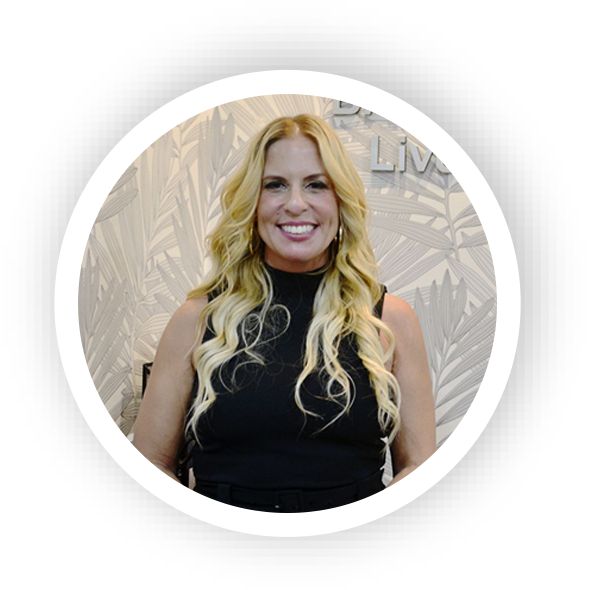 Woman with black clothes and blonde hair, smiling in front of a white wall